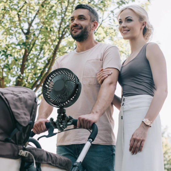 Man and woman standing next to a stroller with a fan attached, outdoors.