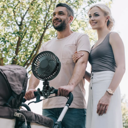 Man and woman standing next to a stroller with a fan attached, outdoors.